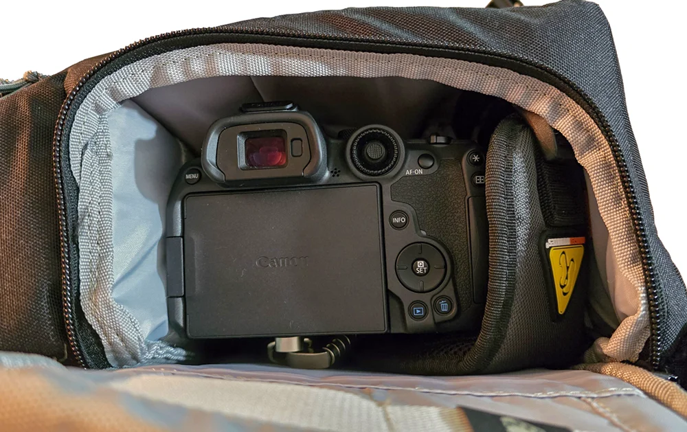 The view through the open side-access port of the sling, showing the back of a Canon R7 camera ready to be lifted out