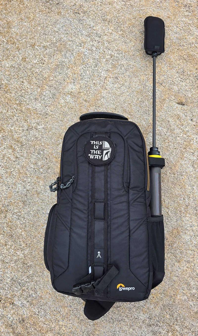 The collapsed selfie stick tucked into the side pocket of a LowePro camera backpack